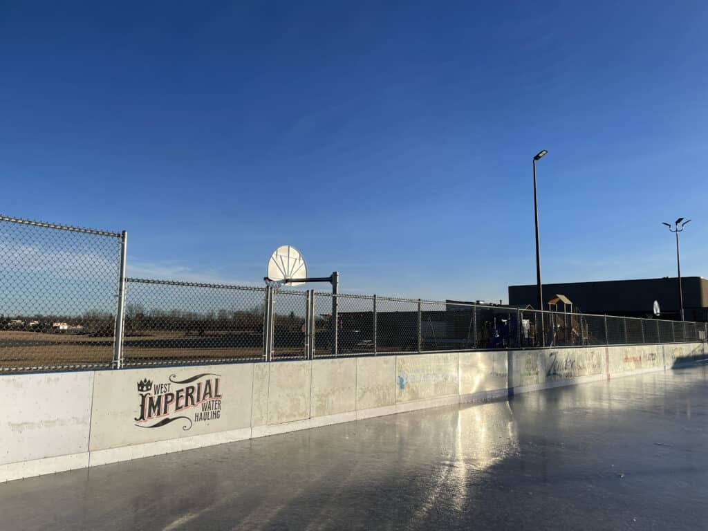 Outdoor ice rink and basketball hoop under blue sky.