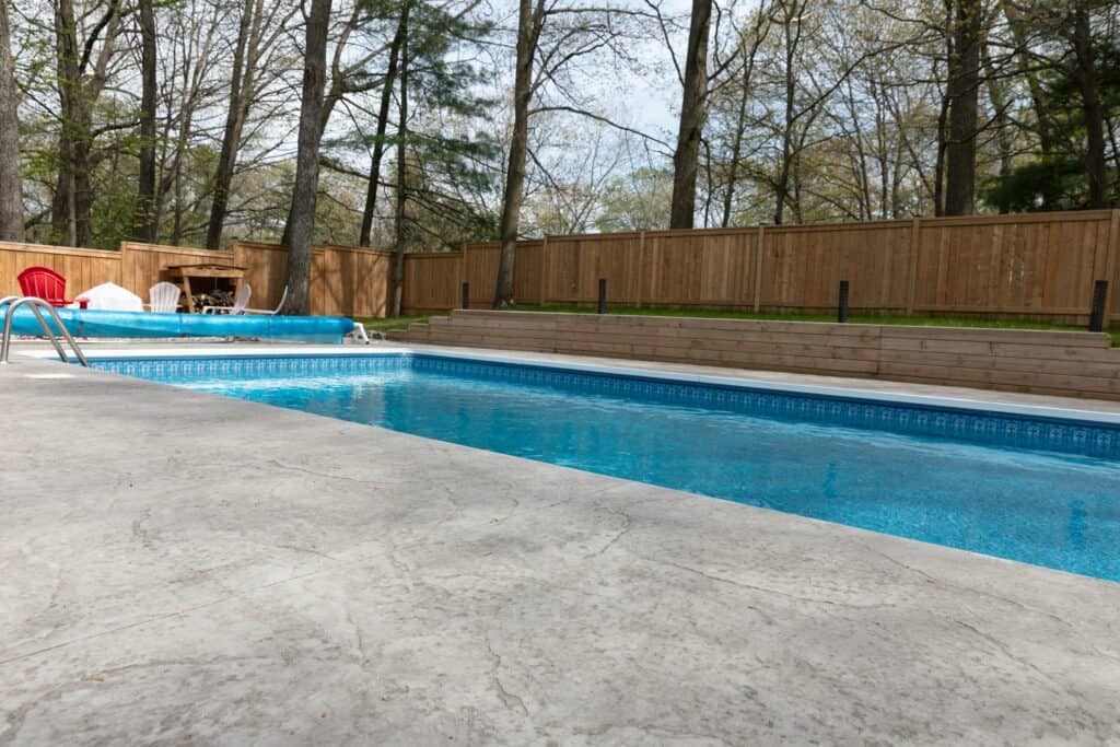 Clear swimming pool surrounded by wooden fence and chairs.